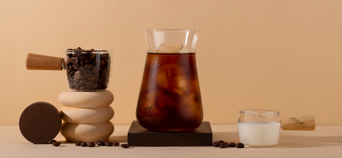 Beaker of black cold brew coffee on ice with coffee beans and milk