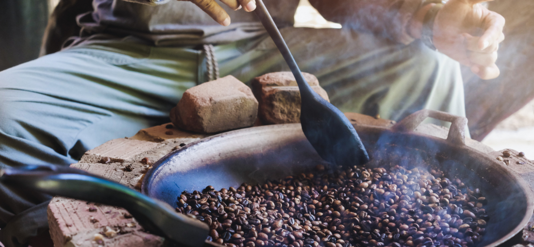 man roasting coffee in a pan over a fire